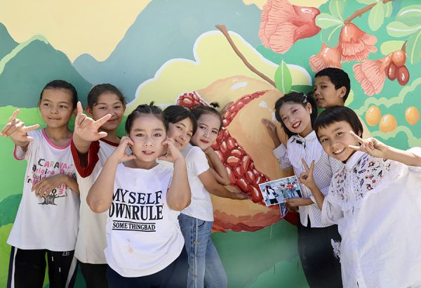 当地青少年在实践团创作的民族团结主题墙绘前合影